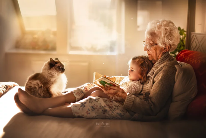 A grandma and her toddler granddaughter read in a comfy spot. 