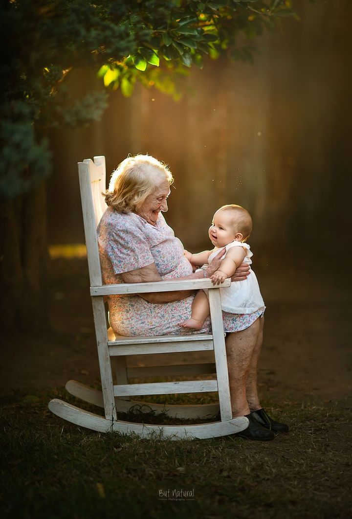 A great-grandma and her great-granddaughter sit in a rocking chair.