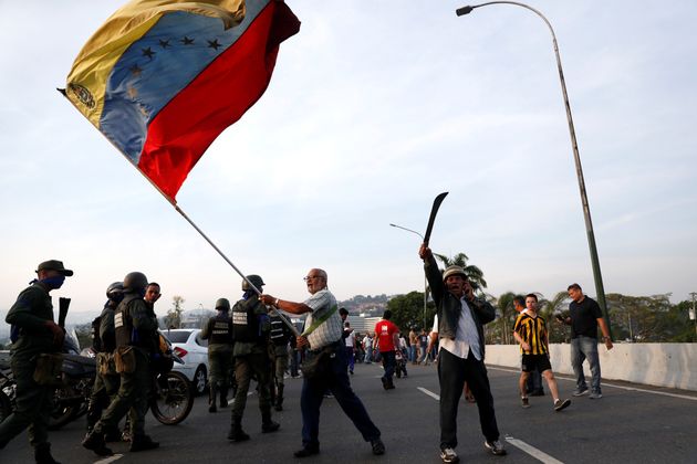 Yποστηρικτές της αντιπολίτευσης ανεμίζουν σημαίες, ενώ ορισμένοι διακρίνονται να κρατούν και μαχαίρια, έξω από την αεροπορική βάση La Carlotta, στο Καράκας, όπου εθεάθη μαζί με ένστολους ο Χουάν Γκουαϊντό.