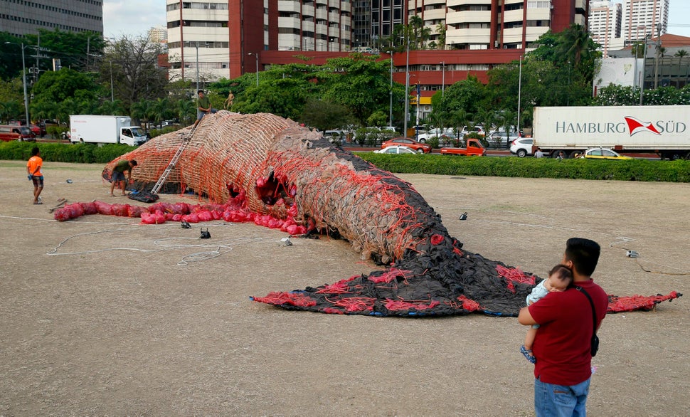 Passersby look on as workers put the finishing touches on "The Cry of the Dead Whale" art installation outside the Cultural C