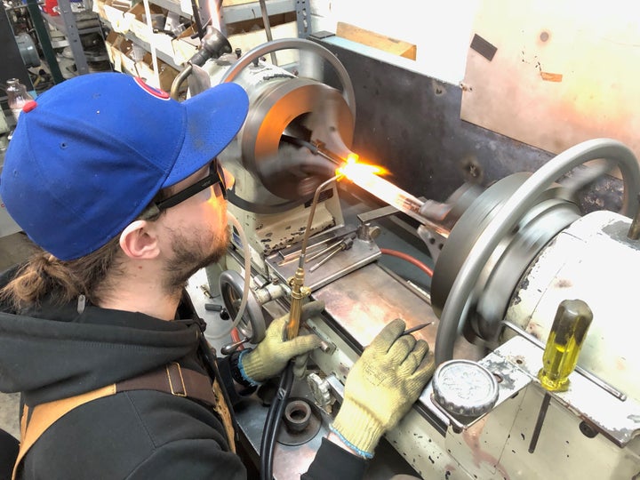 Sam, an employee of Adams & Chittenden Scientific Glass, is repairing a piece of laboratory glassware used for cannabis distillation.