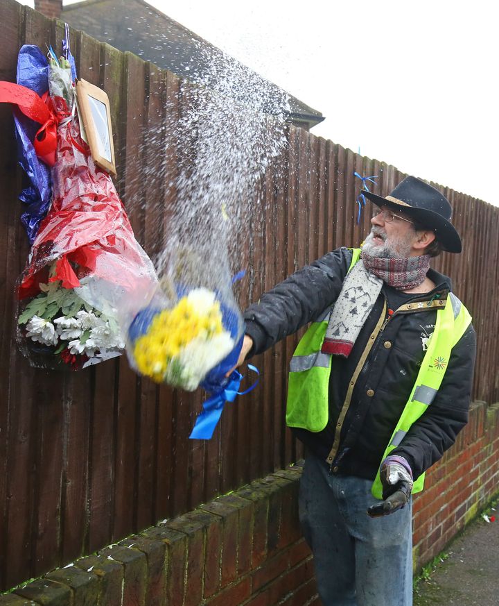 Iain Gordon pulls the flowers down from a fence opposite the house of Osborn-Brooks after it became an unlikely flashpoint of tensions between the grieving family and his neighbours 