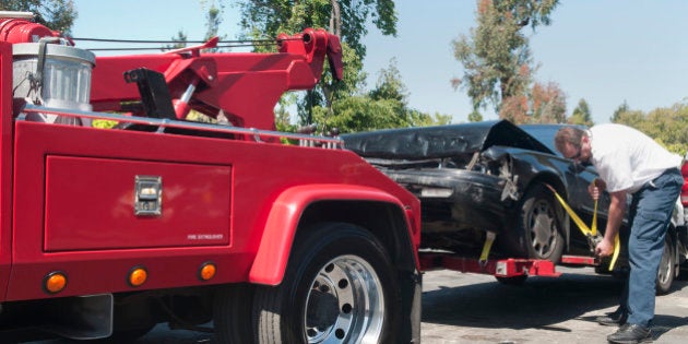 Tow truck driver securely strapping a wrecked car in preparation for towing it.