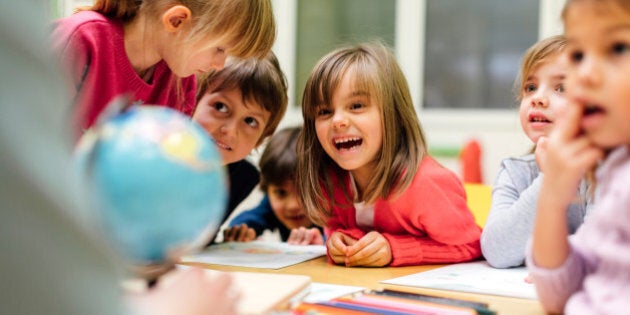 Preschool teacher teaching her children about geography. Using globe and asking the questions. Children sitting by the table and listen teacher carefully. Models in this shot are part of real kindergarten group and their teacher.