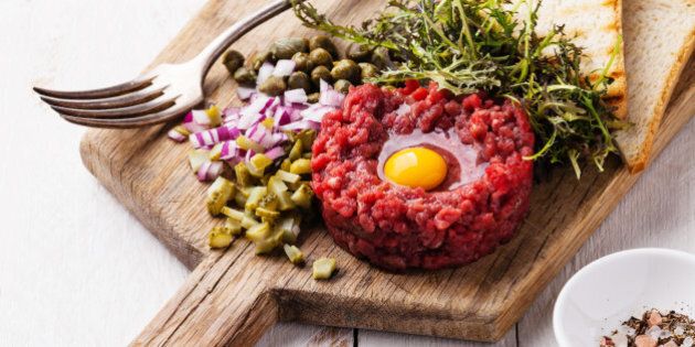 Beef tartare with capers and fresh onion on white wooden background
