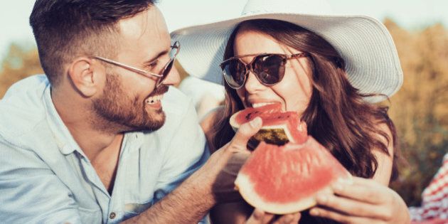 Young couple on a picnic together bite a one piece of watermelon.