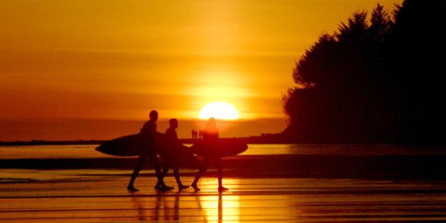 '3 surfers walking with surfboards at sunset on a beach in Tofino, BC, Canada. Camera: Fuji S2'