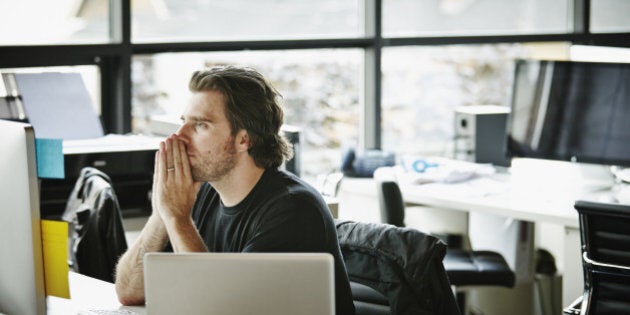 Businessman with hands on chin sitting at office workstation looking at computer monitor