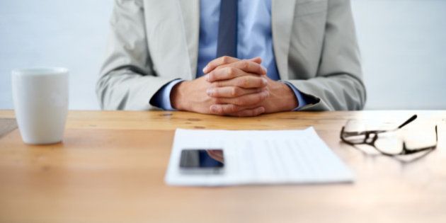 Cropped image of a businessman sitting with hands clasped and paperwork in front of him