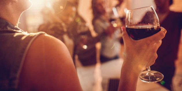 Close up of a businesswoman enjoying in a glass of red wine while being at office party with her colleagues.