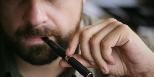 Close up view on the mouth of a bearded man holding and smoking an electronic cigarette
