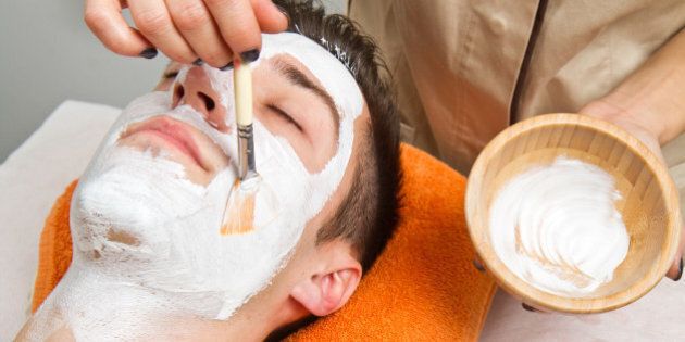 Therapist applying a face mask to a beautiful young man in a spa using a cosmetics brush