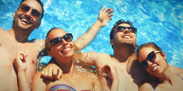Group of friends relaxing in swimming pool on their summer vacation. All wearing sunglasses, smiling and looking at camera. There are two guys and two girls in mid 20's.Shot upside down.