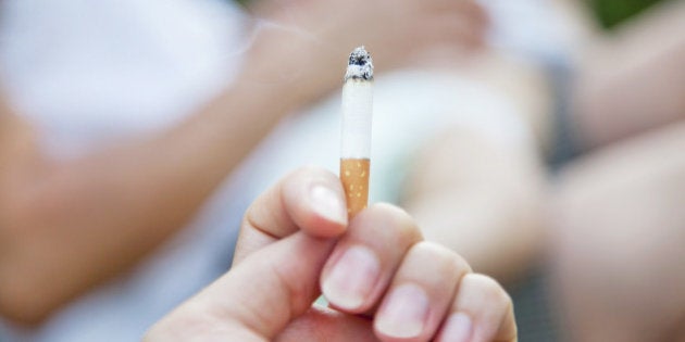 Smoking cigarette,baby with mother in background.