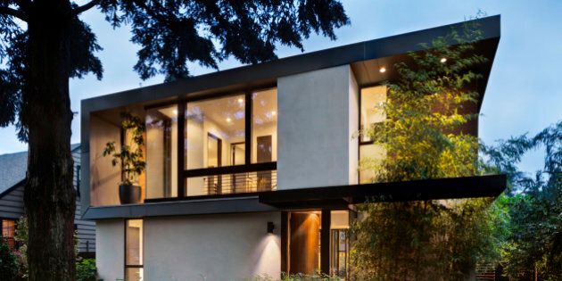 Modern home at twilight with interior and exterior lighting and lush landscaping. Open front door to well lit home interior.