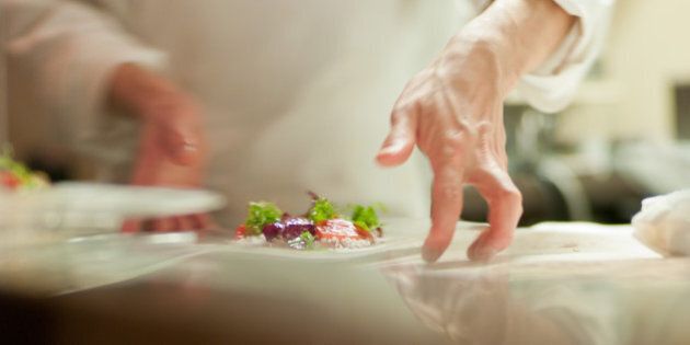 Chef swiftly moves plate in an upscale restaurant before serving patrons.