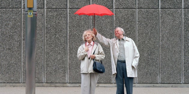 Senior man holding red umbrella over woman, standing on pavement