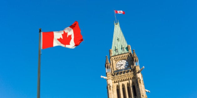 Close up of peace tower (parliament building) with a big canadian flag over blue sky in Ottawa, Canada