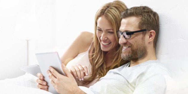 Young woman with man wearing smart glasses using digital tablet on bed