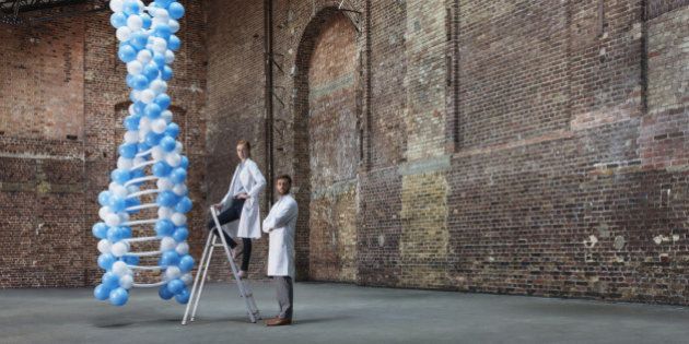 Scientists in empty warehouse with ladder standing next to DNA molecule made of balloons