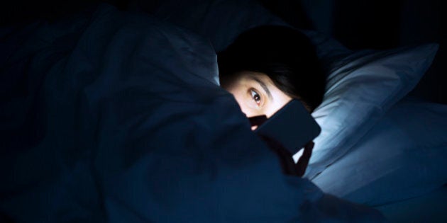 Woman using her phone under blanket in bed at night.