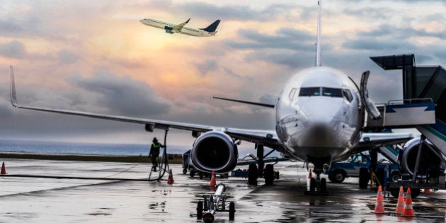 Passenger airplane being refueled and loaded with cargo before the flight near the terminal in an airport at the sunset .