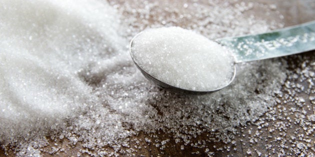 Close-up of granulated sugar in spoon and sugar pile on wooden