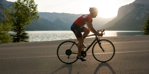 Road biker follows mountain road, sunrise