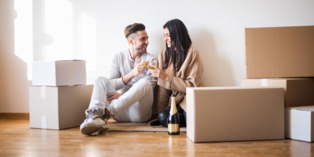 Young couple in love just moved in new apartment and having a toast on the floor before unpacking the boxes.