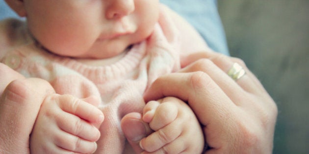 Focus on the hands of a 3 month old baby girl holding the fingers of her father. Vintage style color filter.