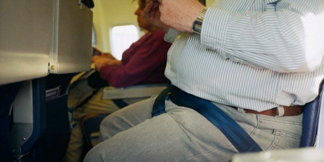 A close up of an overweight man's stomach on a plane.