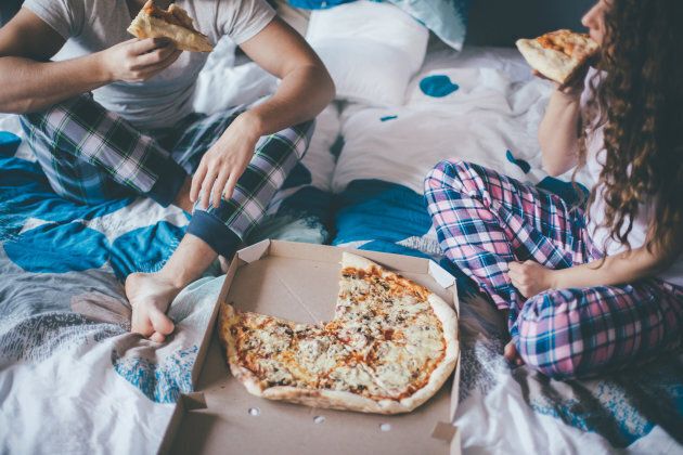 Couple having pizza in the bed in bedroom.