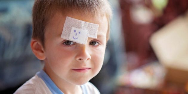 Close portrait of a boy with band aid on forehead, injured, sad but smiling