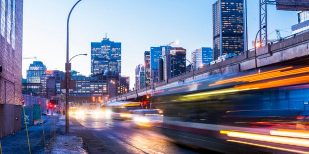 This is a horizontal, color, royalty free stock photograph of downtown rush hour traffic along Autoroute Bonadventure in Montreal an urban travel destination in Quebec, Canada. The city buildings are illuminated in the background as dusk turns to night. Buses and cars drive past on the street in a motion blur of light streaks. Photographed with a Nikon D800 DSLR camera.