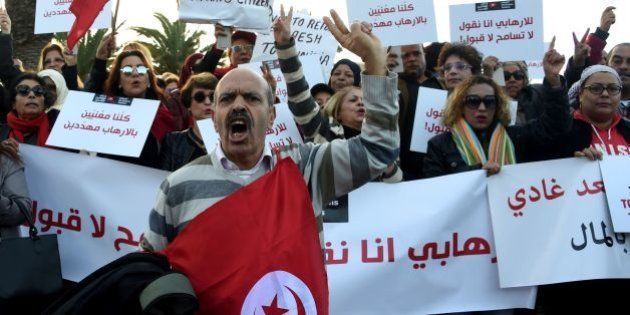 Tunisians shout slogans during a demonstration outside parliament against allowing Tunisians who joined the ranks of jihadist groups to return to the country, in the capital Tunis on December 24, 2016. The writing in Arabic reads: ''we are all under threat by terrorism''. / AFP / FETHI BELAID (Photo credit should read FETHI BELAID/AFP/Getty Images)
