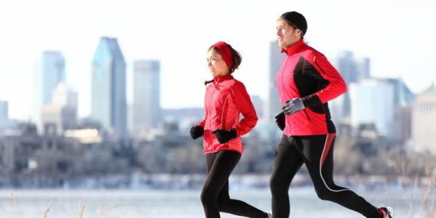 Runners running in winter snow with city background. Healthy multiracial young couple woman and man Montreal skyline, Quebec Canada