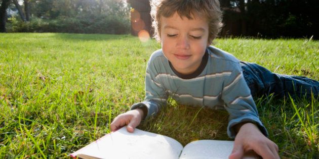 Mixed race boy reading book in grass