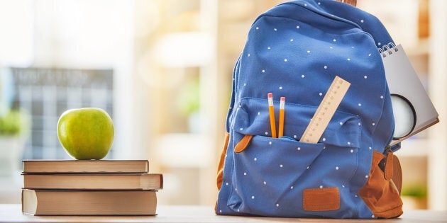 Back to school and happy time! Apple, pile of books and backpack on the desk at the elementary school.