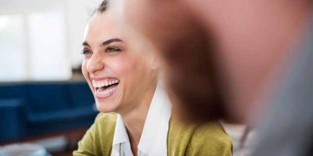 Cheerful businesswoman looking away while laughing at creative office with colleague in foreground