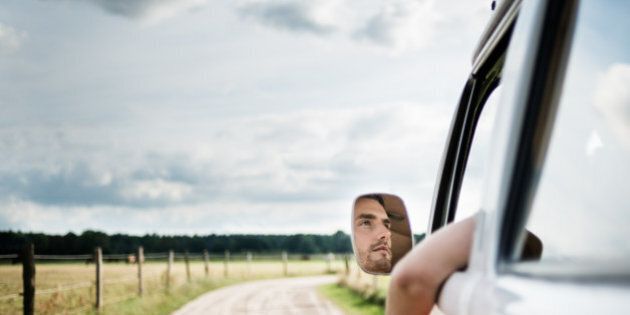 Face of a young man reflecting in a mirror of an old bus driving along a country road.