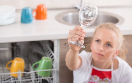 78838163 - pretty blonde woman holding wine glass high above dishwasher and checking cleanness