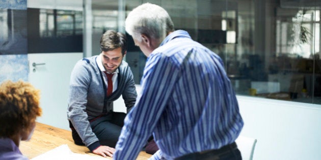 Mature businessman analyzing blueprint with colleagues in board room at office