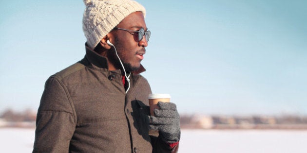 Portrait free young african man enjoying drinking coffee over blue sky in cold winter day looking profile