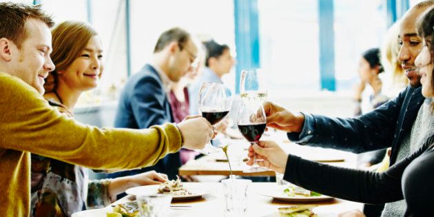 Group of friends toasting with wine glasses at table in restaurant