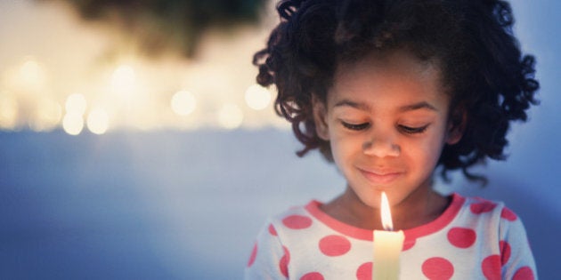 African American girl in pajamas holding lit candle