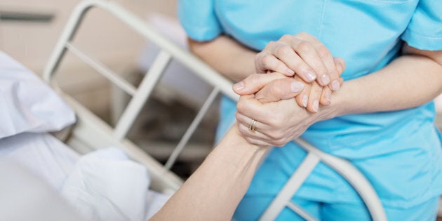 Midsection of female nurse holding senior woman's hand. Caring medical professional is with patient. She is consoling elderly woman in hospital.