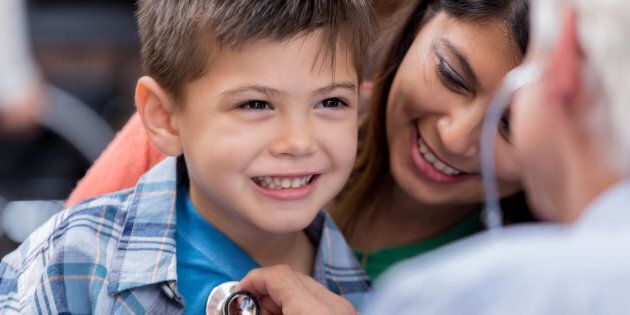 Cute elementary age boy smiles while pediatrician checks his heart and lungs with a stethoscope.