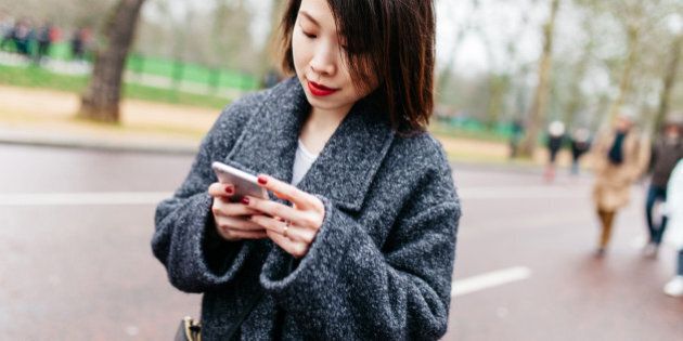 Young asian girl checking smartphone on the street