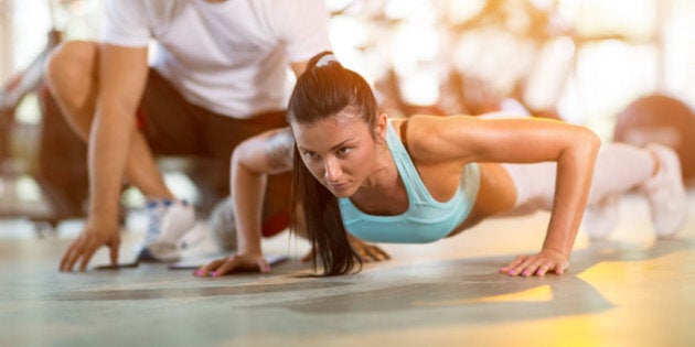 Young woman doing push ups under supervision of a trainer at gym