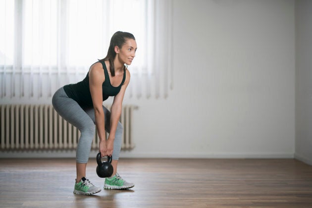 Beautiful young woman doing kettlebell deadlifts at home.
